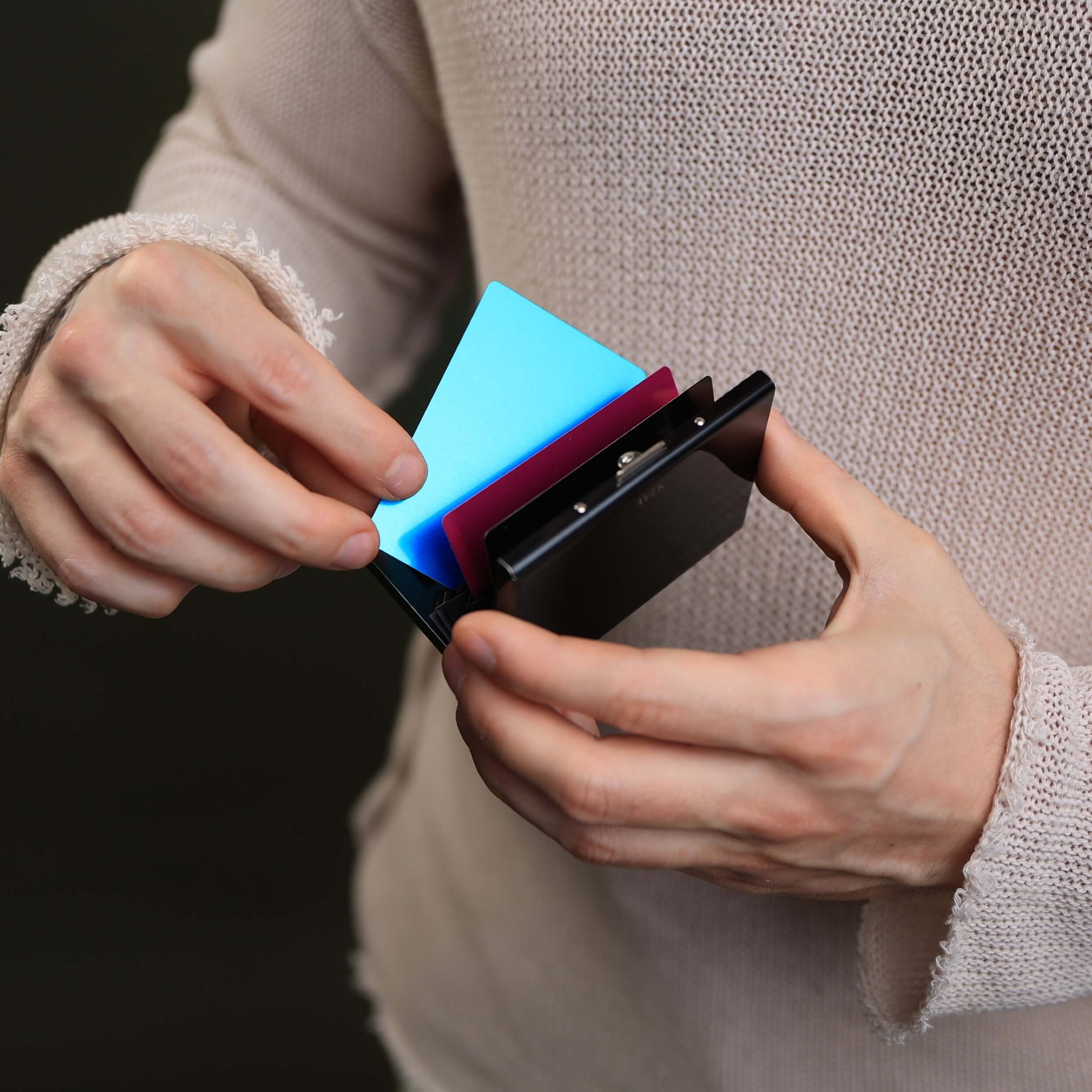 Otwarte czarne stalowe etui na karty RFID z rozłożonymi kartami płatniczymi w dłoniach